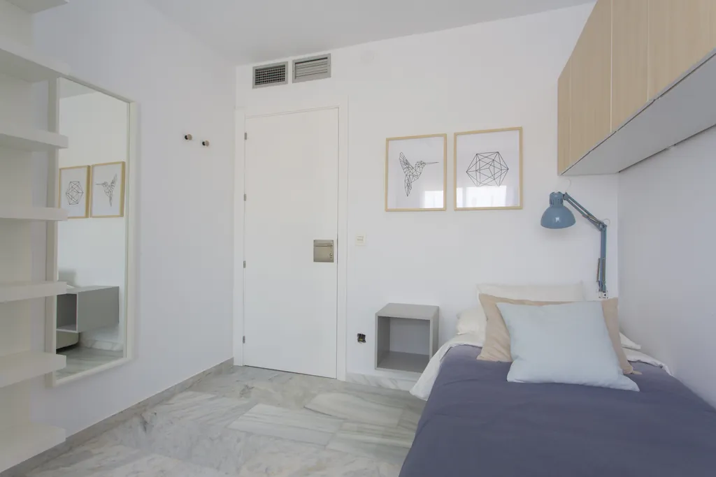Habitación individual renovada con cama, flexo y armarios de madera clara