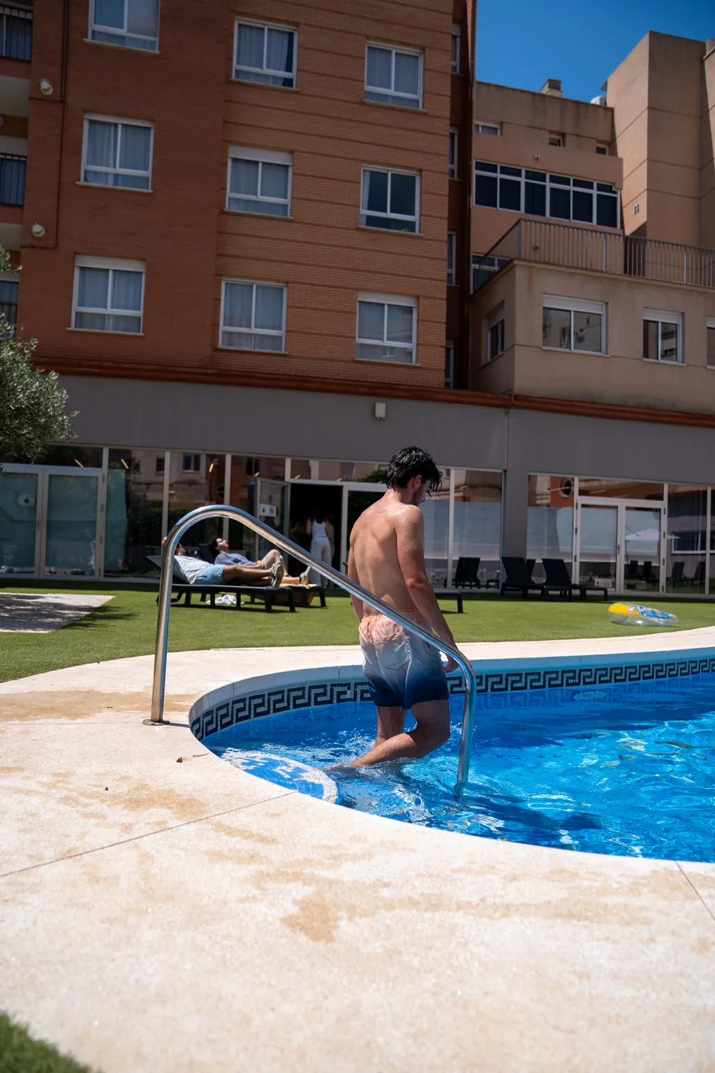 Un residente entra en la piscina del patio de la residencia en un día de sol